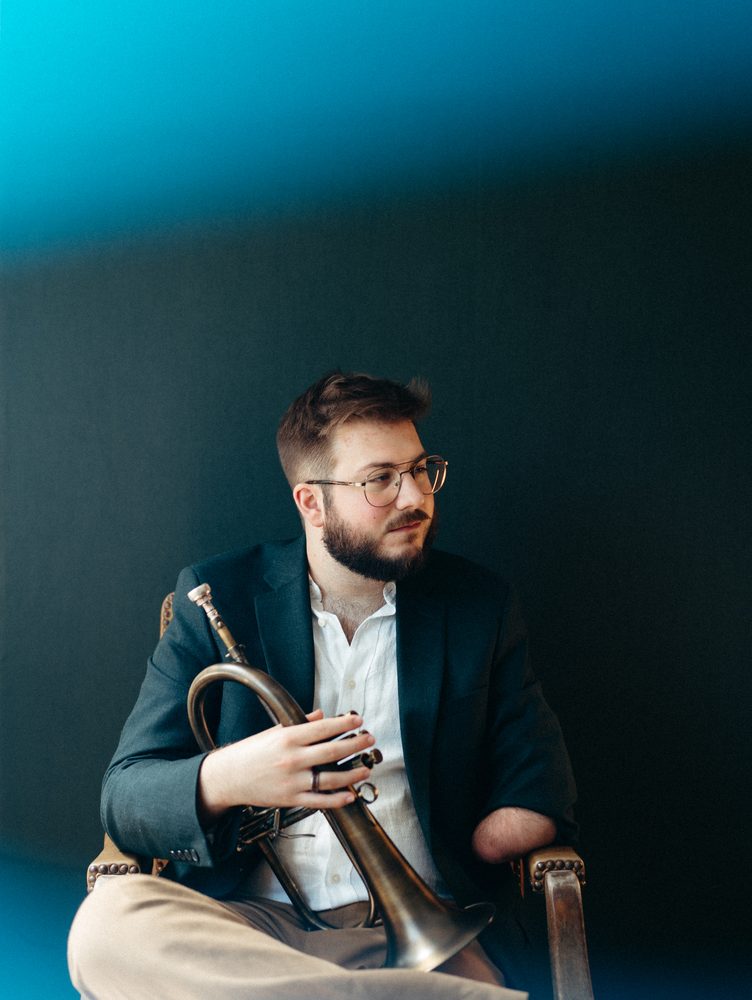 Christian seated with a flugelhorn under a teal glow