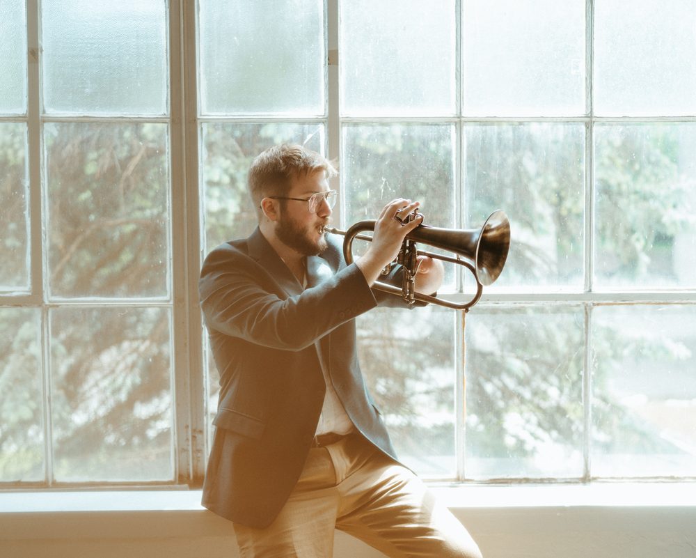 Christian playing flugelhorn in front of tall paned windows, warm light